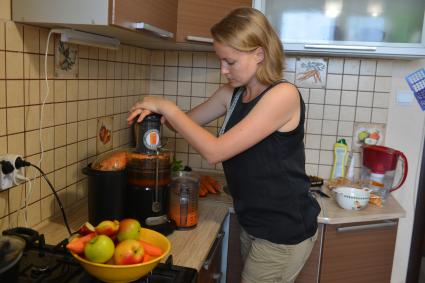 Девушка готовит свежевыжатый сок из яблок и моркови.