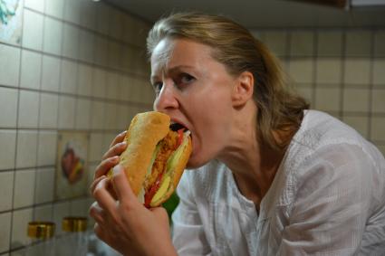 Девушка ест украдкой бутерброд на кухне.