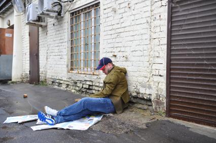 Пьяный мужчина сидит на земле у кирпичной стены.