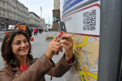 Девушка с помощью мобильного телефона считывает QR-код с информационной таблички.