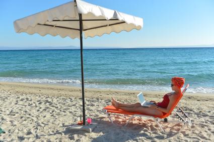 Греция. На снимке: туристка с ноутбуком на пляже.