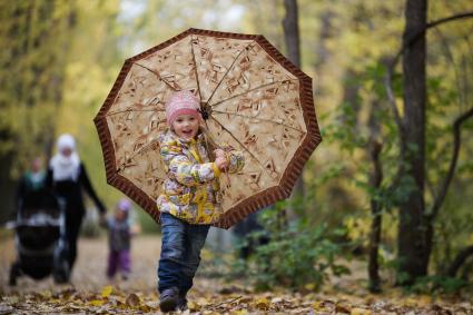 Ребенок с зонтом гуляет по парку.