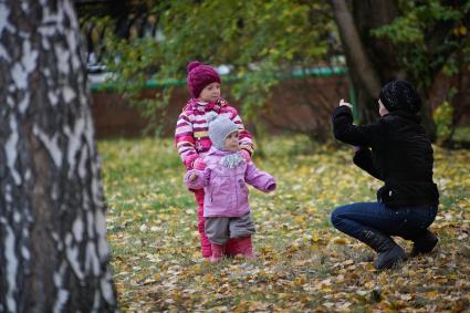 Женщина фотографирует детей в осеннем парке.