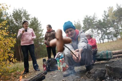 Компания молодых людей жарят хлеб и сосиски на костре в осеннем лесу.