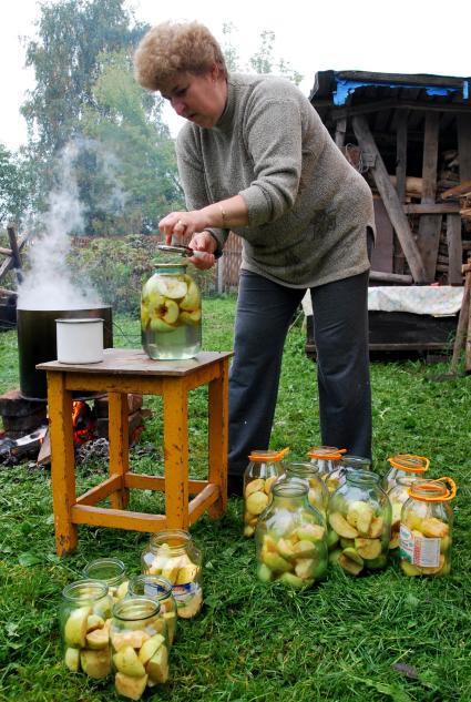 Женщина закатывает банки с мочеными яблоками.