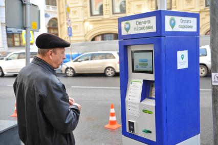 На снимке: мужчина с сигаретой стоит у терминала оплаты парковки.