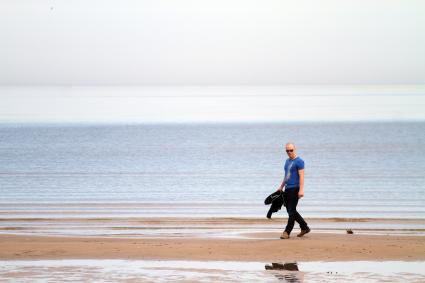 Мужчина идет по берегу Балтийского моря в Юрмале.