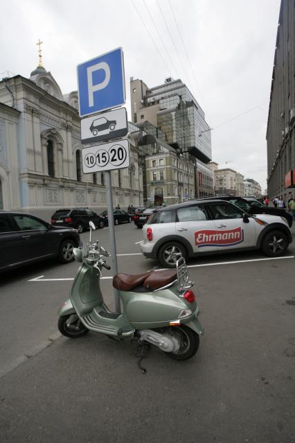 Припаркованный скутер у дорожного знака `Платная стоянка`