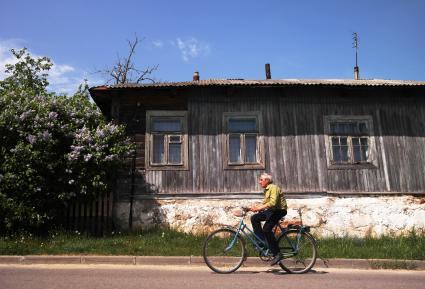 Мужчина едет на велосипеде возле деревянного дома.