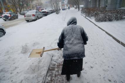 Снегопад в Екатеринбурге. На снимке: женщина убирает снег с пешеходной зоны деревянной лопатой.