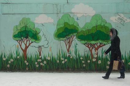 Снегопад в Екатеринбурге. На снимке: женщина идет мимо стены с нарисованными летними деревьями.