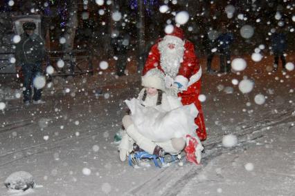 Дед Мороз везет Снегурочку на санках.