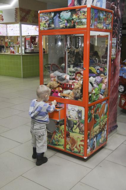 Ребенок увлеченно пытается достать игрушку из игрового автомата.