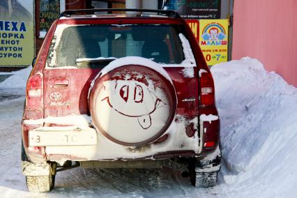 Смайлик нарисованный снегом на запаске автомобиля.