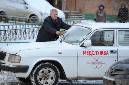 Мужчина очищает автомобиль от снега.