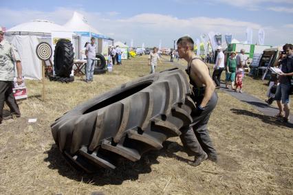 Межрегиональный агропромышленный форум `День сибирского поля - 2013`. Конкурс силачей. Мужчина поднимает огромное колесо.
