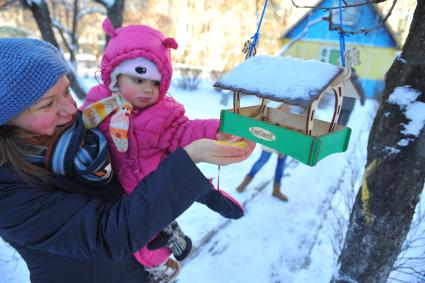 Женщина с ребенком сыпет зерно в кормушку для птиц.