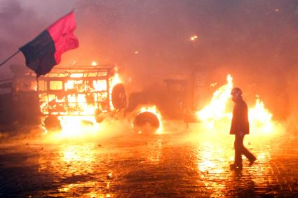 Протестующий в шлеме на фоне горящего автобуса.