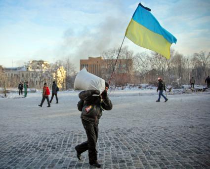 Протестующий с украинским флагом несет мешок для укрепления баррикад.