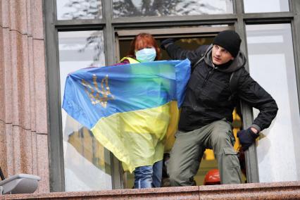 Протестующие в окне с украинским флагом.