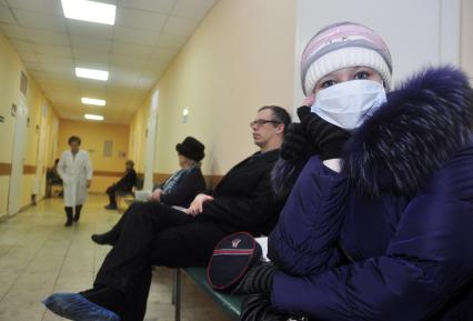 Девушка в медицинской повязке сидит в ожидании приема врача в поликлинике.