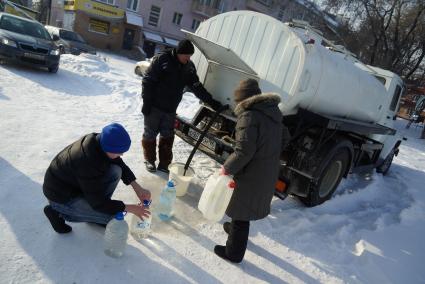 Мужчина набирает питьевую воду в пластиковую тару, рядом пенсионерка с пустой канистрой у водовоза.