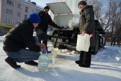 Мужчина набирает питьевую воду в пластиковую тару, рядом пенсионерка с пустой канистрой у водовоза.