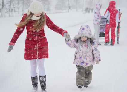 Девушка с ребенком идут под снегопадом по улице.