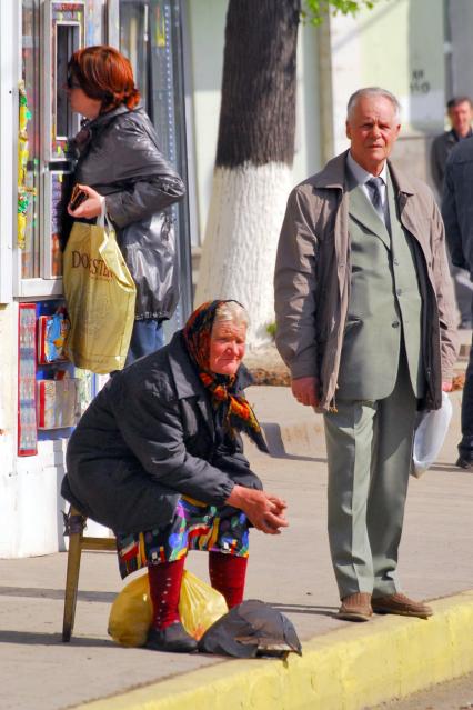 Стоящий пенсионер и сидящая на стуле пенсионерка на улице перед ларьком.