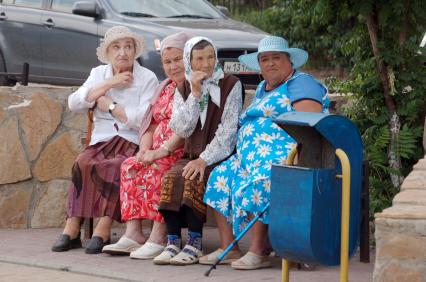 Нарядные пенсионерки сидят летом на лавочке.