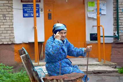 Пенсионерка крутит пальцем у виска, на лавочке перед подъездом жилого дома.