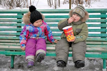Празднование масленицы в Туле. На снимке: дети сидят на лавочке, ребенок ест попкорн.
