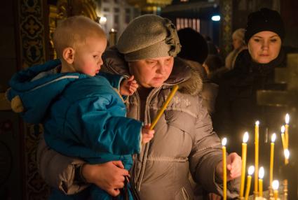 Крещение в Самаре. Женщина ставит свечку держа на руках ребенка.