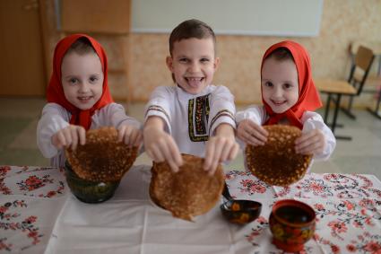 Масленица. На снимке: девочки-близняшки и мальчик в русских народных костюмах угощают блинами.