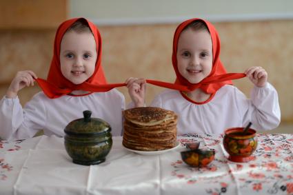 Масленица. На снимке: девочки-близняшки сидят за столом с блинами.