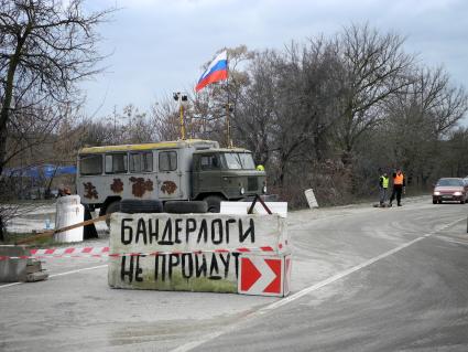 Блок-пост на въезде в город. Надпись на бетонных плитах: `Бандерлоги не пройдут`, российский флг на грузовом автомобиле.