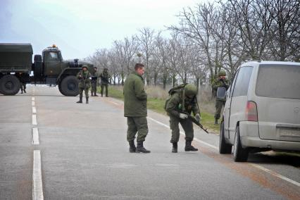 Блок-пост на дороге ввиде грузового автомобиля посередение дороги контролируемый военными. Досмотр проезжающего транспорта.