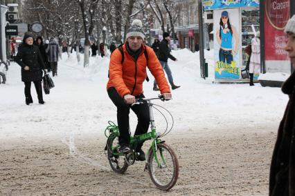 Мужчина на велосипеде едет по заснеженной улице.