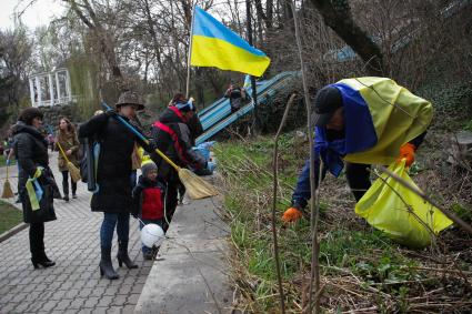 Люди убирают территорию парка под флагом Украины.