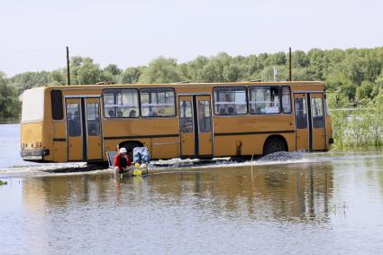Рейсовый автобус едет по затопленной части дороги мимо рыбака.