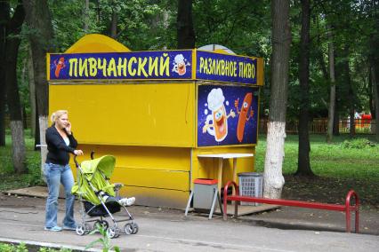 Мама с ребенком в коляске прогуливается на фоне пивного киоска в Автозаводском парке отдыха.