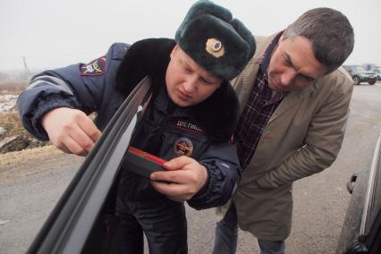 Сотрудник ДПС ГИБДД замеряет тонировку стекол автомобиля.