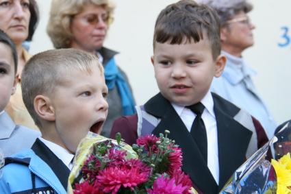 Зевающий ребенок с букетом цветов на школьной линейке.