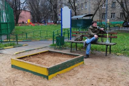 Молодой человек курит кальян на детской полщадке.