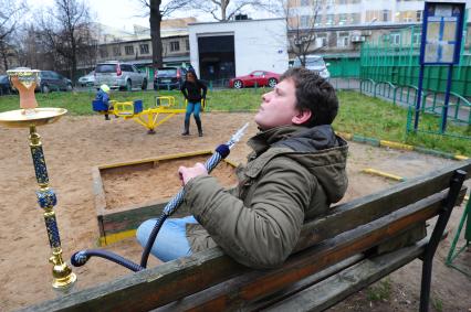 Молодой человек курит кальян на детской полщадке.