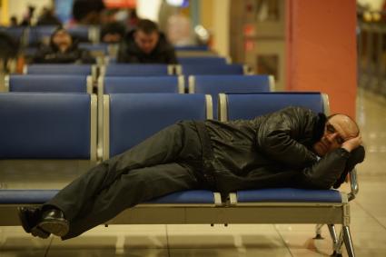 Мужчина спит на креслах в зале ожидания аэропорта.