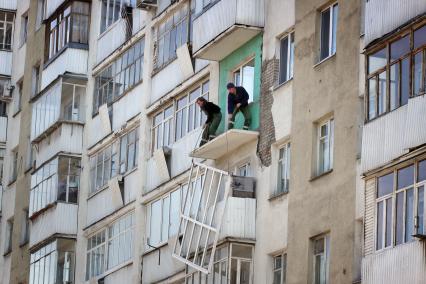 Рабочие готовят балкон к застеклению, поднимают несущие конструкции.