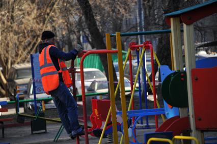 Гастарбайтер красит турник на детской площадке.