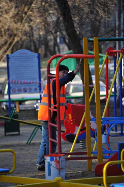 Гастарбайтер красит турник на детской площадке.