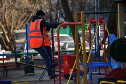 Гастарбайтер красит турник на детской площадке.